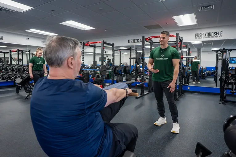Trainer guiding an older client through a seated arm raise