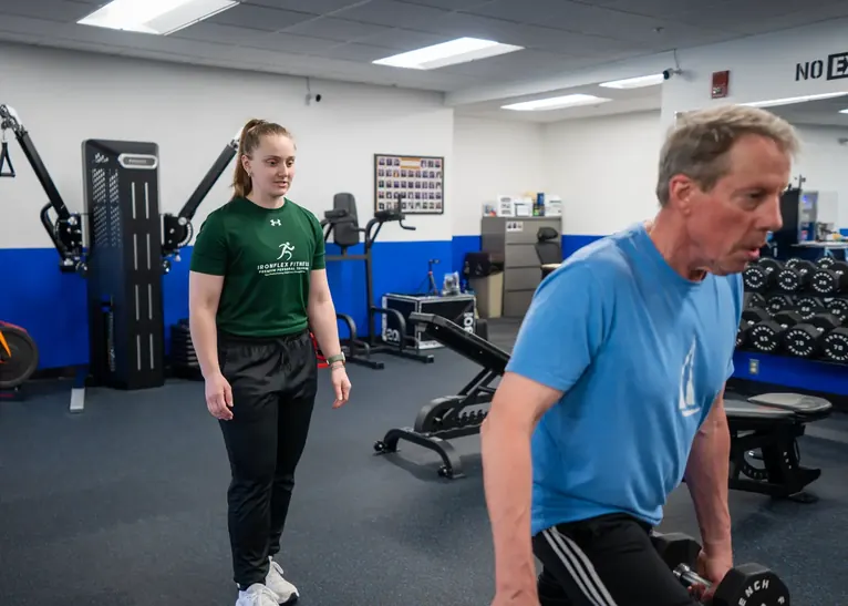 Trainer coaching an older client through a loaded carry