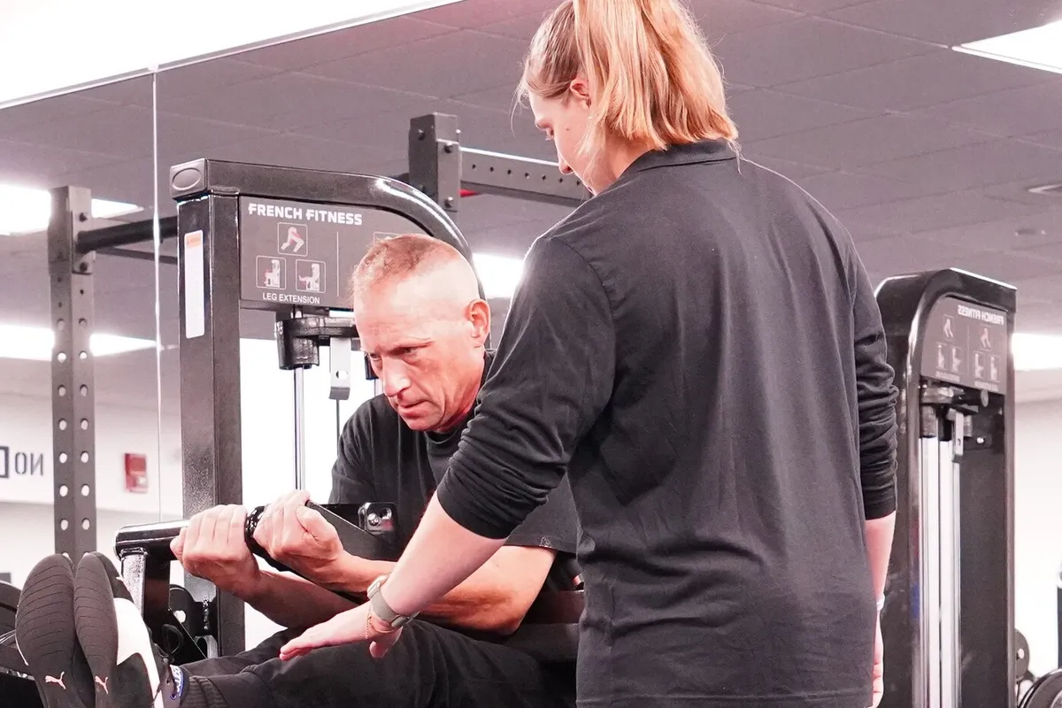 Gina correcting a client's form on the leg extension