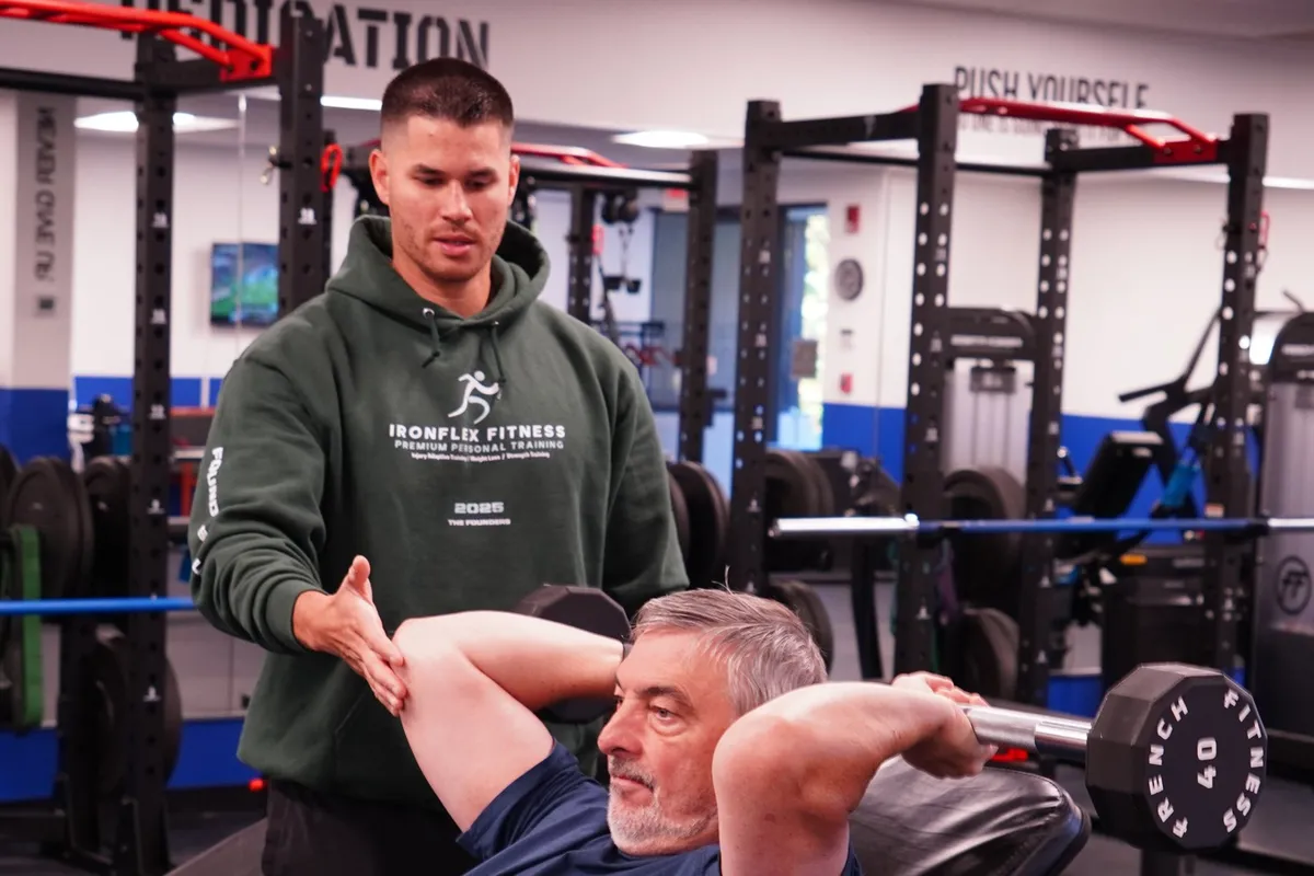 Coach spotting an older client through a dumbbell pullover