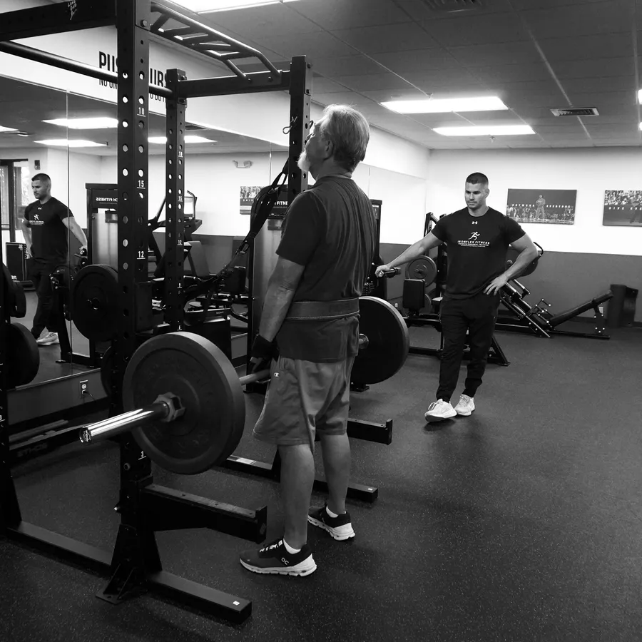 Connor Crouse coaching a client through a barbell squat at IronFlex