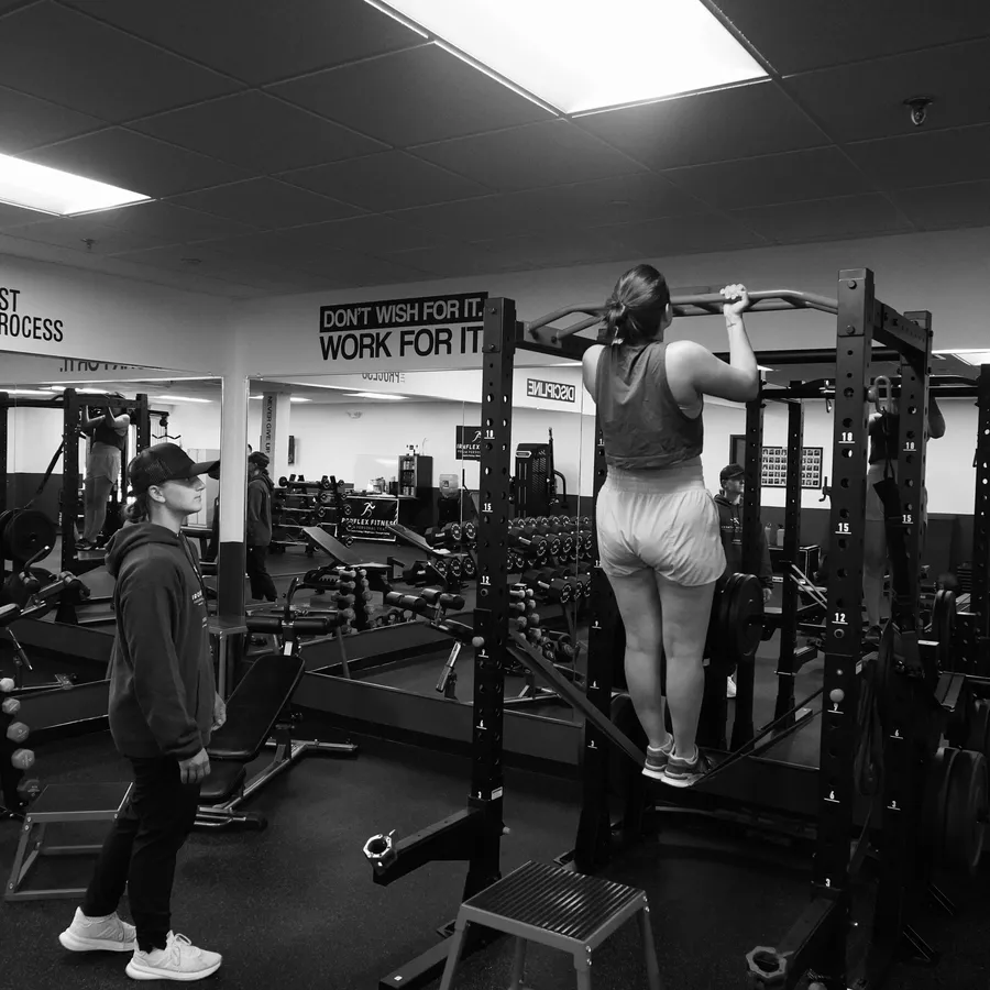 Gina Carroll spotting a client on the pull-up bar at IronFlex